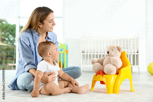 Funny teddy bear sitting on potty and mother with her child at home