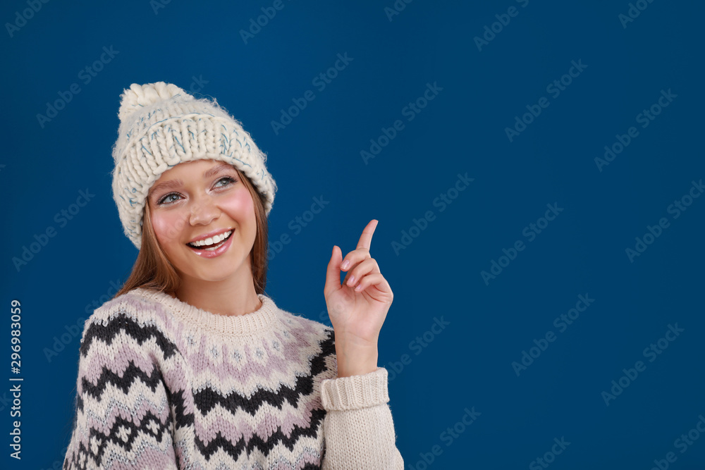 Young woman in warm sweater and hat on blue background, space for text. Winter season Young woman in warm sweater and hat on blue background, space for text. Winter season