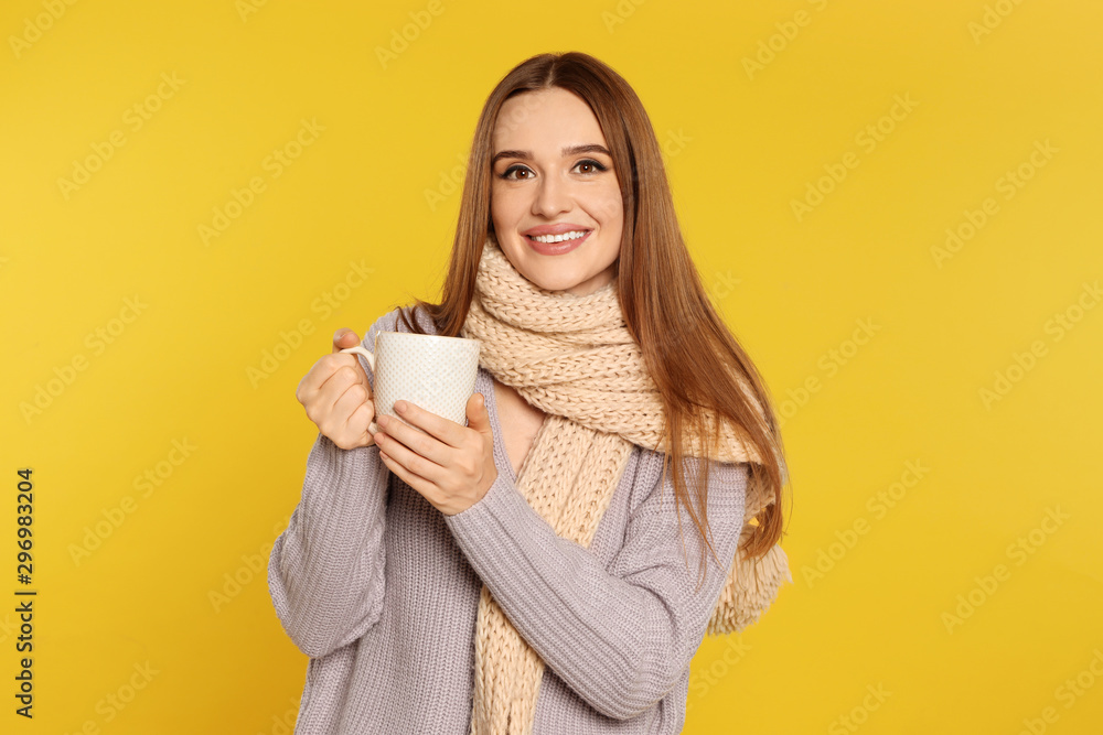 Beautiful young woman in sweater with drink on yellow background. Winter season Beautiful young woman in sweater with drink on yellow background. Winter season