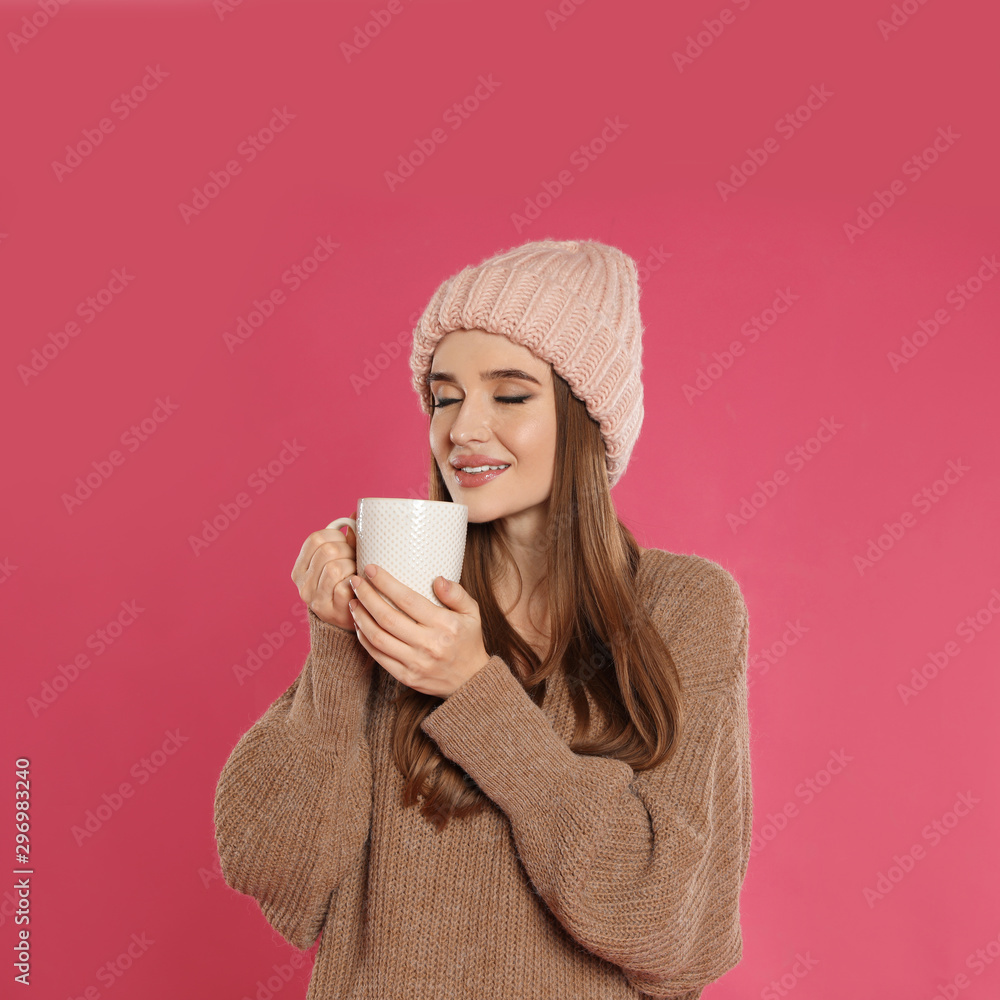Beautiful young woman in hat and sweater with drink on pink background. Winter season Beautiful young woman in hat and sweater with drink on pink background. Winter season