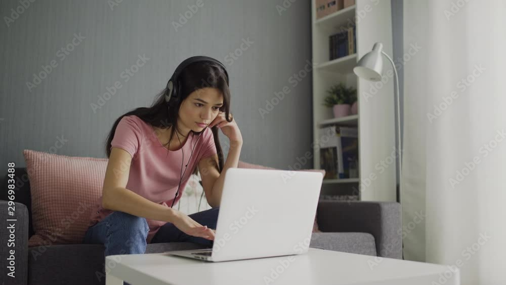 Young woman in headphones looking on screen laptop and typing on keyboard Young woman in headphones looking on screen laptop and typing on keyboard