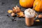 Pumpkin spice latte with whipped cream and cinnamon stick in glass cup on grey table. Space for text