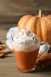 Pumpkin spice latte with whipped cream in glass cup on wooden table