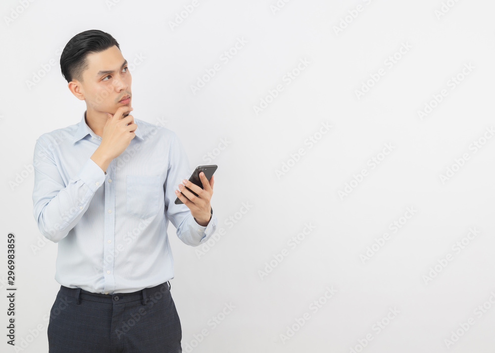 Young handsome asian business man holding a black smartphone and thinking an idea while looking up isolated on white background. Young handsome asian business man holding a black smartphone and thinking an idea while looking up isolated on white background.