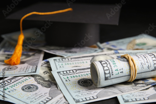 Dollar banknotes and student graduation hat on table, closeup. Tuition fees concept photo