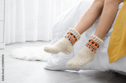 Woman wearing knitted socks on bed indoors, closeup. Warm clothes