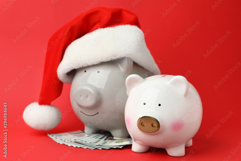 Piggy banks with Santa hat and dollar banknotes on red background Piggy banks with Santa hat and dollar banknotes on red background