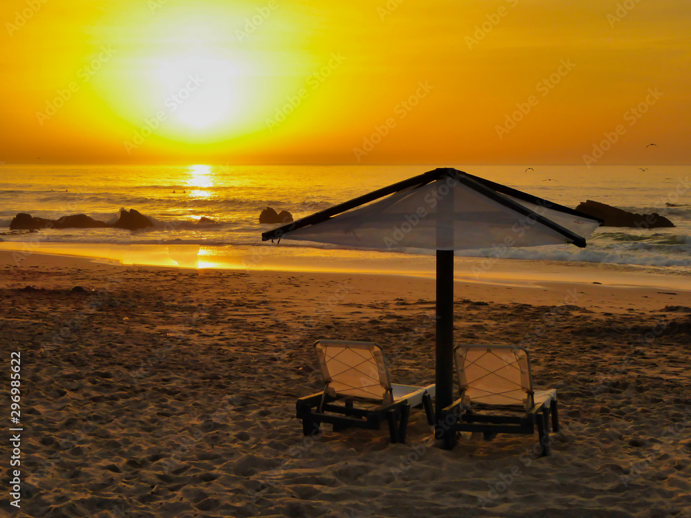 The famous beach called: Praia do Guincho in Portugal during sunset with sun chairs and a parasol
