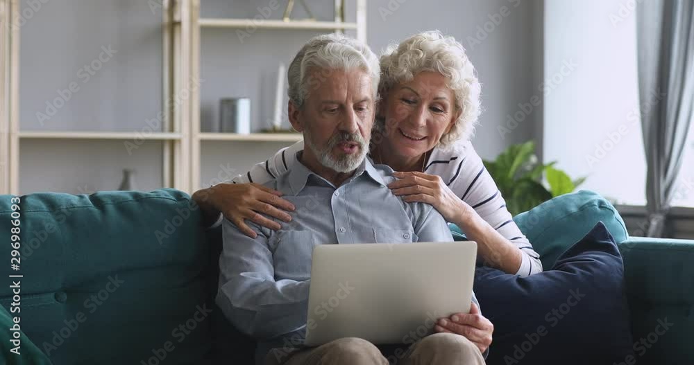 Happy older grandfather using laptop talk with grandmother at home