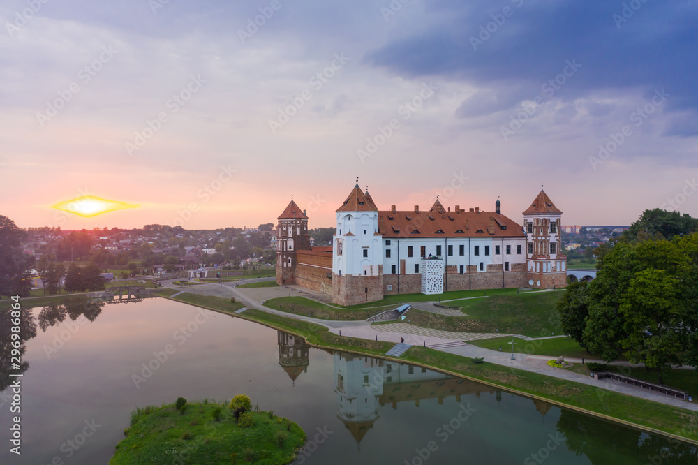 Mirsky Castle and its reflection in the lake in summer. Sunset in cloudy weather with rain clouds