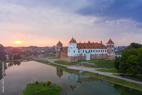 Mirsky Castle and its reflection in the lake in summer. Sunset in cloudy weather with rain clouds