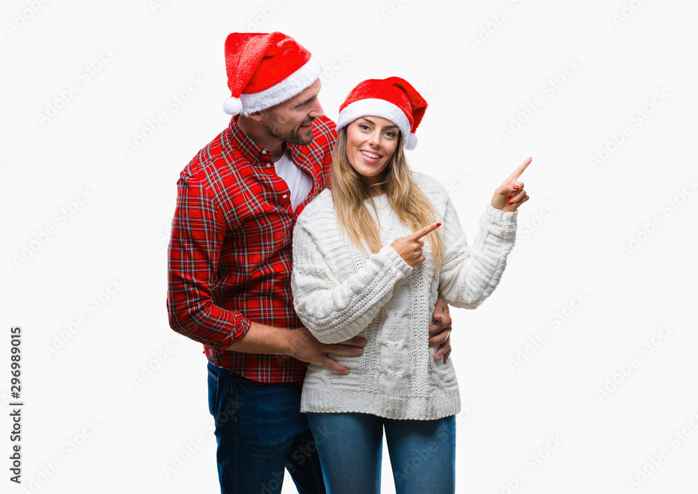 Young couple in love wearing christmas hat over isolated background smiling and looking at the camera pointing with two hands and fingers to the side. Young couple in love wearing christmas hat over isolated background smiling and looking at the camera pointing with two hands and fingers to the side.
