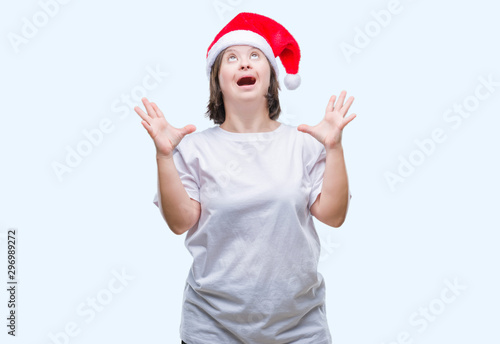 Young adult woman with down syndrome wearing christmas hat over isolated background crazy and mad shouting and yelling with aggressive expression and arms raised. Frustration concept.