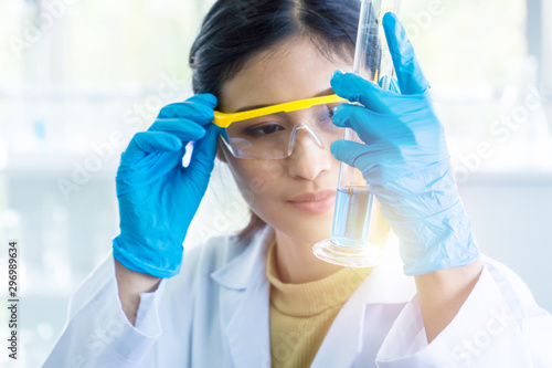 Female Asian scientist with rubber glove looking at blue chemical liquid in the glass tube. Science biochemical and pharmaceutical concept.