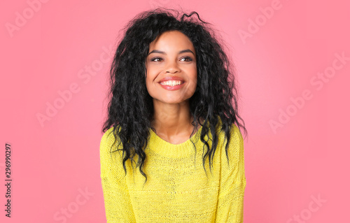 Sunny girl. Beautiful tanned woman with Afro hairstyle is laughing while posing in a knitted light yellow sweater, looking to the right and smiling at the camera.