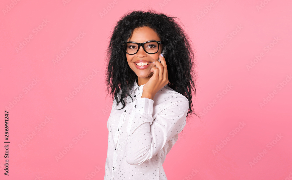 Discussing my next meeting. Happy Afro-American business woman in a white blouse is posing in profile holding a smartphone near her left ear, smiling and looking to the camera.