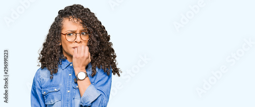 Quadro em tela Young beautiful woman with curly hair wearing glasses looking stressed and nervous with hands on mouth biting nails