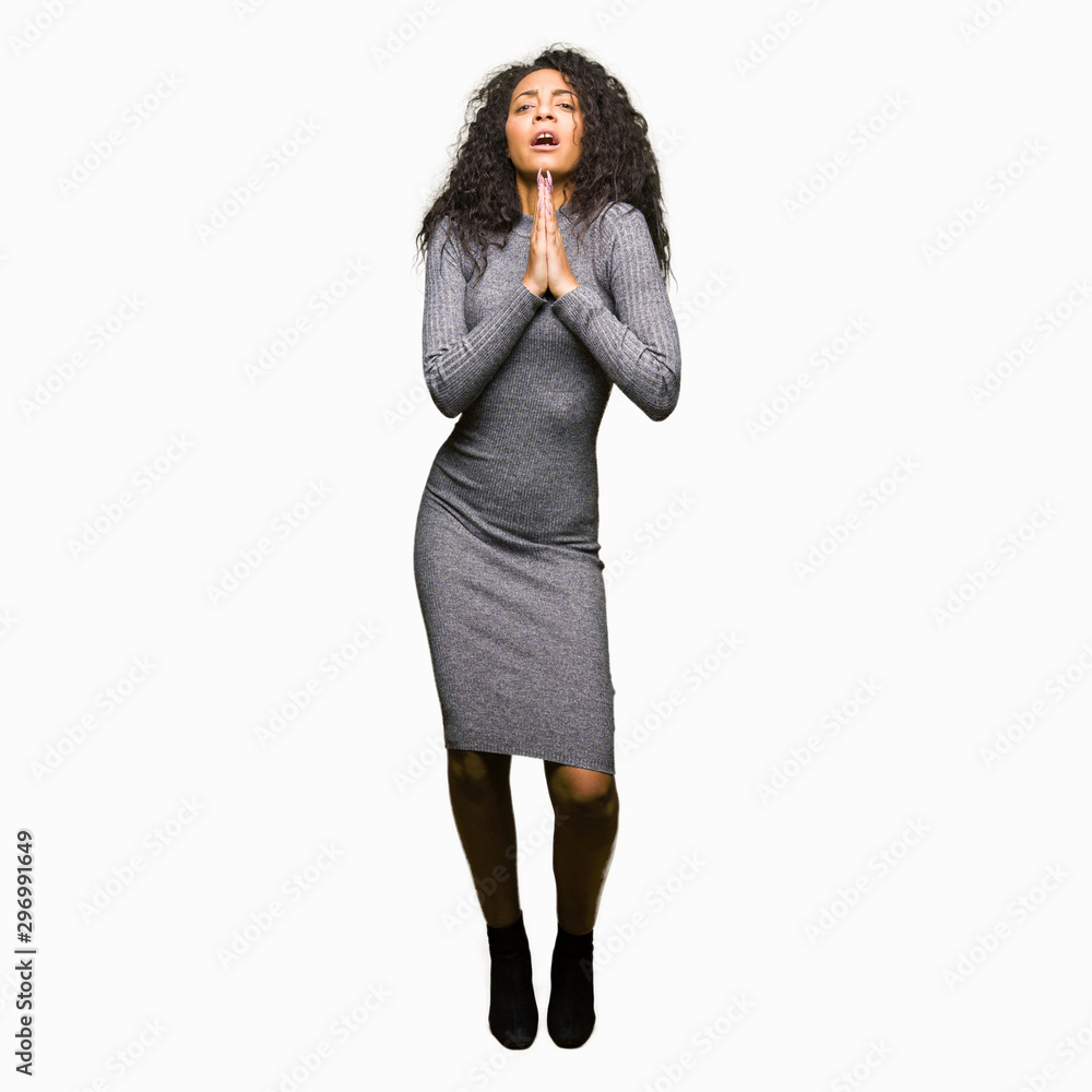 Fototapeta premium Young beautiful girl with curly hair begging and praying with hands together with hope expression on face very emotional and worried. Asking for forgiveness. Religion concept.