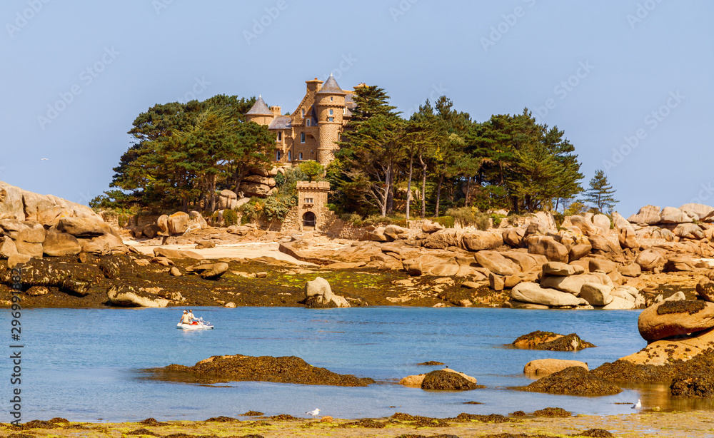 View of the island of Costaérès with its castle Costaéres( built in 1885), rocky coastline, reddish granite rock formations on the Pink Granite Coast (Côte de Granit Rose). Brittany, France.	