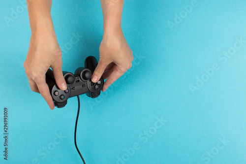 Female hands hold a gamepad on a blue background. Weekend concept, gaming hobby. Copy space.