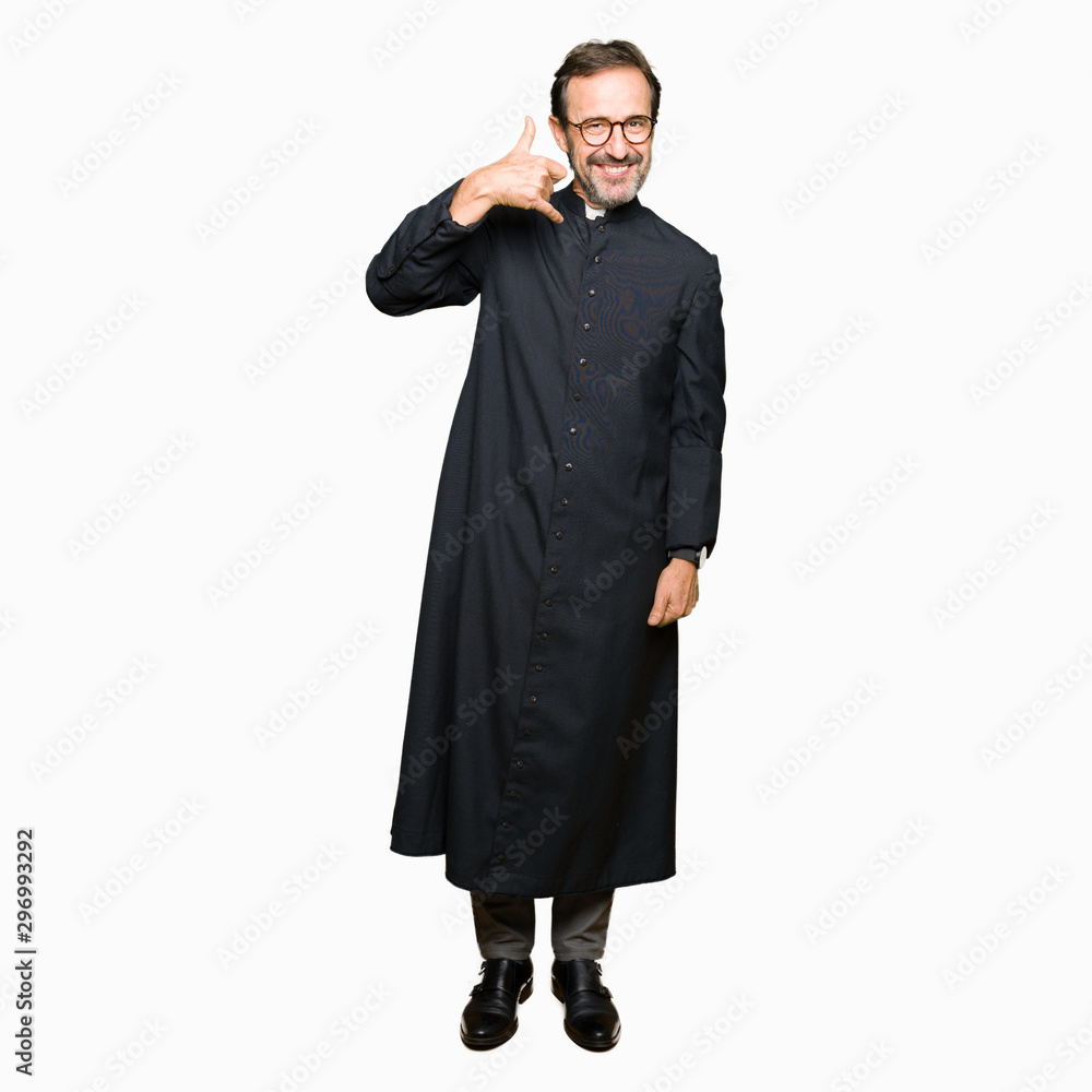 Middle age priest man wearing catholic robe smiling doing phone gesture with hand and fingers like talking on the telephone. Communicating concepts. Middle age priest man wearing catholic robe smiling doing phone gesture with hand and fingers like talking on the telephone. Communicating concepts.