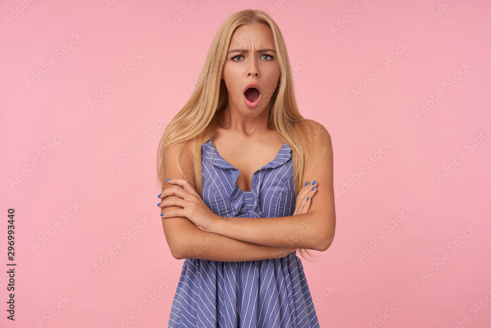 Goggle young blonde female with loose hair holding hands folded on her chest while posing over pink background, looking at camera dazedly and frowning her face Goggle young blonde female with loose hair holding hands folded on her chest while posing over pink background, looking at camera dazedly and frowning her face
