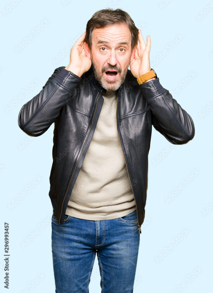 Middle age handsome man wearing black leather jacket Trying to hear both hands on ear gesture, curious for gossip. Hearing problem, deaf Middle age handsome man wearing black leather jacket Trying to hear both hands on ear gesture, curious for gossip. Hearing problem, deaf