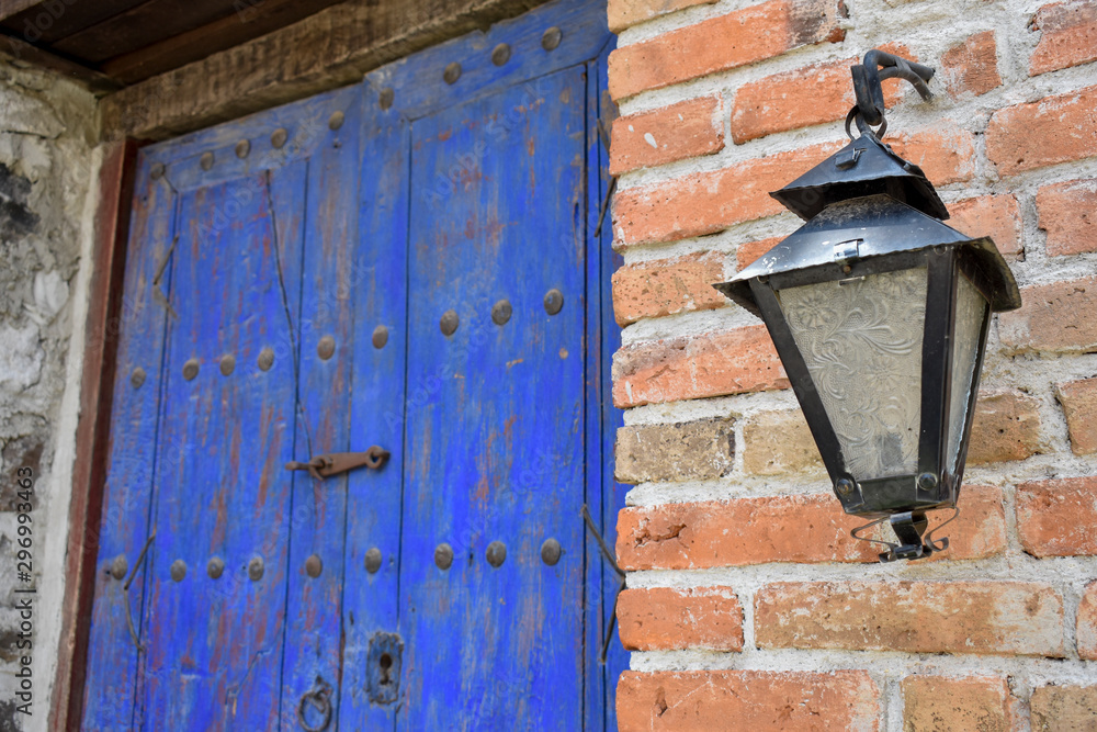 Fachada de casa de ladrillos con puerta rústica de madera pintada de color azul con cerradura antigua y un farol 