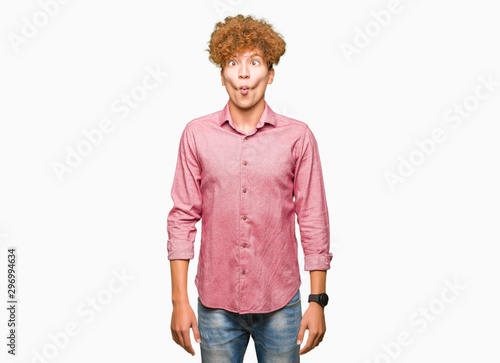 Young handsome business man with afro hair making fish face with lips, crazy and comical gesture. Funny expression. photo