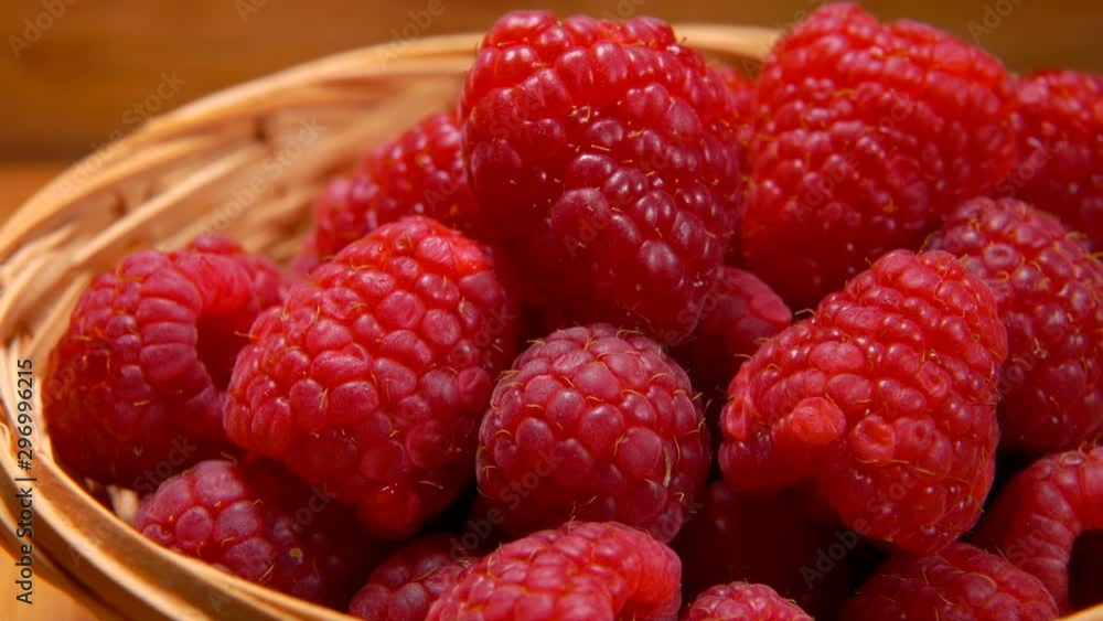 Hand takes a big juicy appetizing raspberries out of wicker basket Hand takes a big juicy appetizing raspberries out of wicker basket