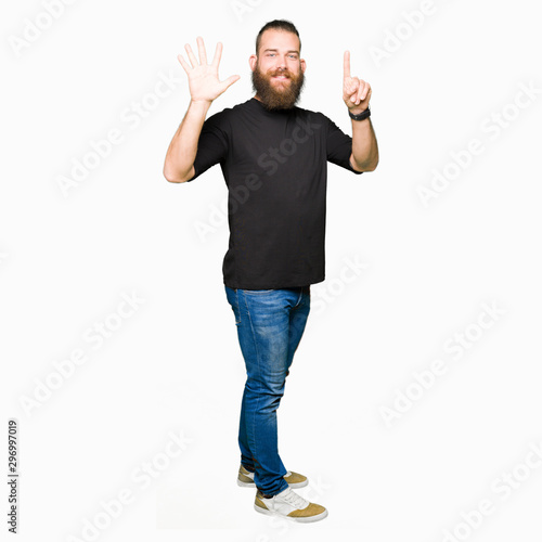 Young blond man wearing casual t-shirt showing and pointing up with fingers number six while smiling confident and happy.