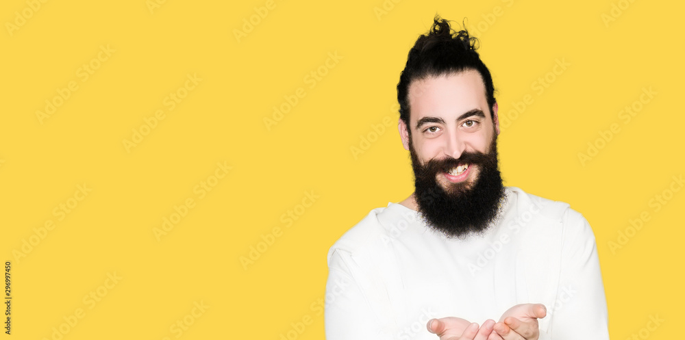 Obraz premium Young hipster man with long hair and beard wearing sporty sweatshirt Smiling with hands palms together receiving or giving gesture. Hold and protection