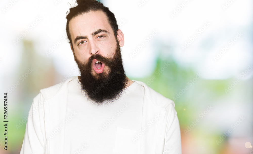 Young hipster man with long hair and beard wearing sporty sweatshirt In shock face, looking skeptical and sarcastic, surprised with open mouth Young hipster man with long hair and beard wearing sporty sweatshirt In shock face, looking skeptical and sarcastic, surprised with open mouth