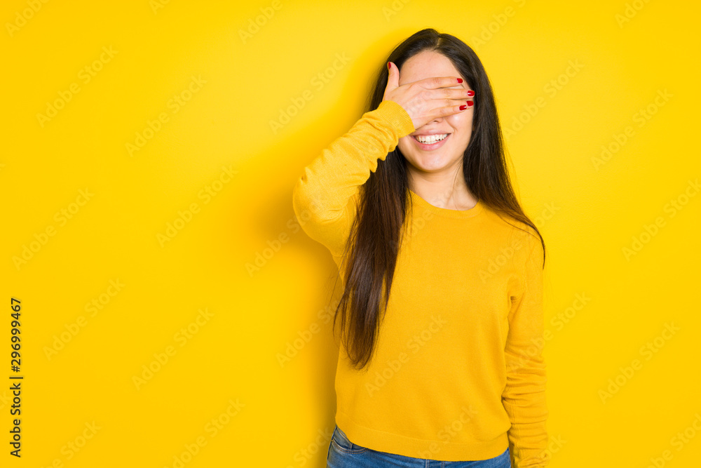 Beautiful brunette woman over yellow isolated background smiling and laughing with hand on face covering eyes for surprise. Blind concept. Beautiful brunette woman over yellow isolated background smiling and laughing with hand on face covering eyes for surprise. Blind concept.