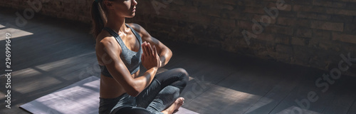 Calm fit sporty healthy mindful woman sit in lotus pose doing yoga exercise breathing fresh air meditating in gym lit with sunlight, stress free concept, horizontal banner website design, copy space