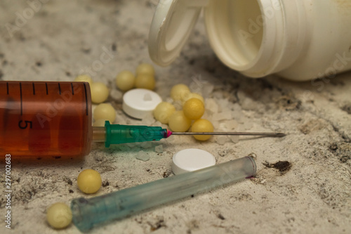 Syringe with a solution (heroin) on a concrete surface with tablets. Drug addiction. Social problem.