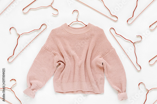 Pale pink knitted sweater with metallic hangers on white background. Autumn and winter clothes. Store, sale, fashion concept.