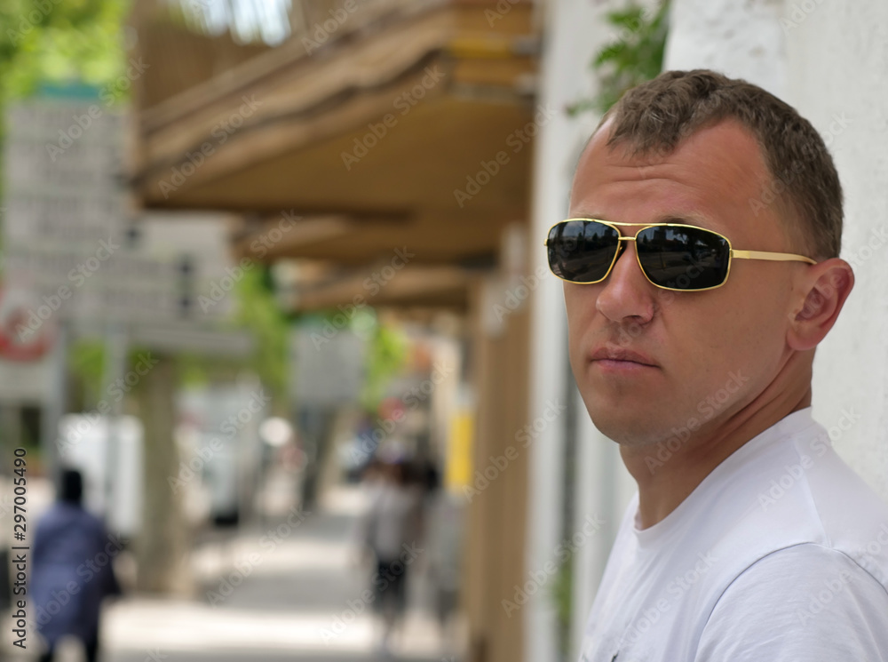 Portrait of a young man on a sunny day near the wall on a street background, looking at the camera Portrait of a young man on a sunny day near the wall on a street background, looking at the camera