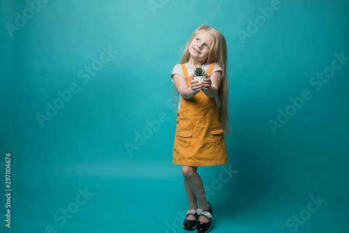 A little girl holding pots with a green plant on a blue background. Children and nature. Preserve nature
