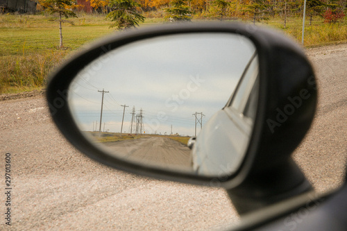 Close-up of a Rearview Mirror Framing Road with big Eletricity Poles.