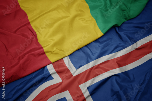 waving colorful flag of iceland and national flag of guinea.