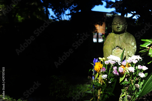 Buddha in pietra illuminato dal raggio di sole con fiori 