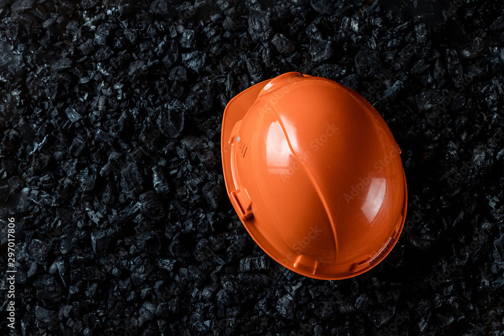 An orange helmet of a miner lies on a heap of coal, open pit coal mining, copy space. Fossil fuels, environmental pollution.