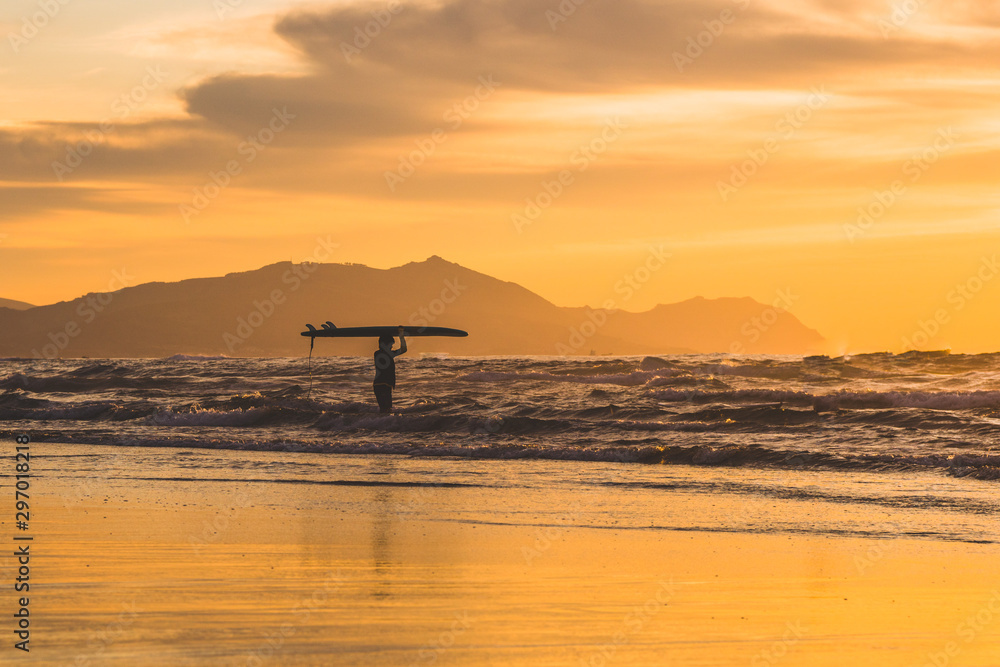 Surfer holding the surfboard on his head. Beautiful dramatic sunset in Basque Country, north of Spain