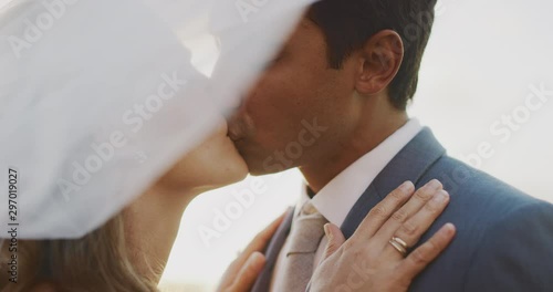 Happy multi ethnic couple getting married, couple kissing at their wedding at sunset under a white veil photo