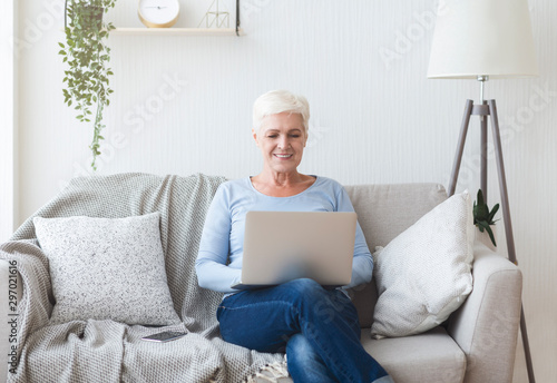 Ambitious senior lady using laptop on sofa at home