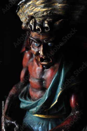 Demone, scultura in legno colorato, esce dall'oscurità
