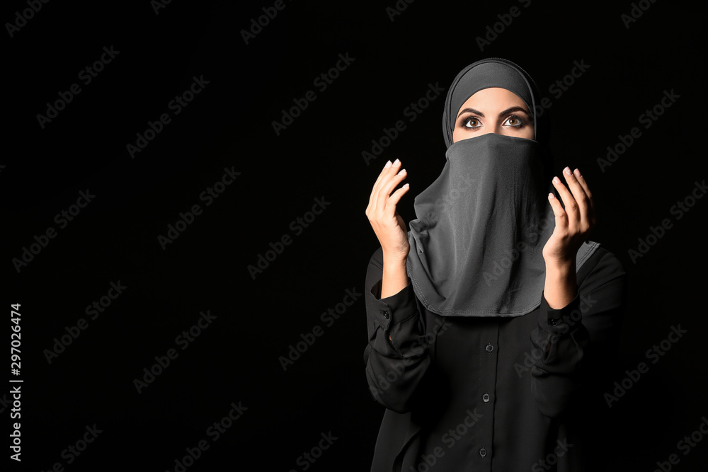 Beautiful Muslim woman praying against dark background