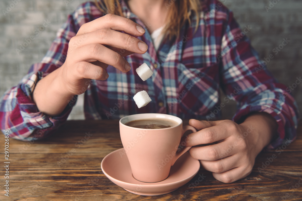 Woman dropping sugar cubes into cup with hot coffee at table, closeup Woman dropping sugar cubes into cup with hot coffee at table, closeup