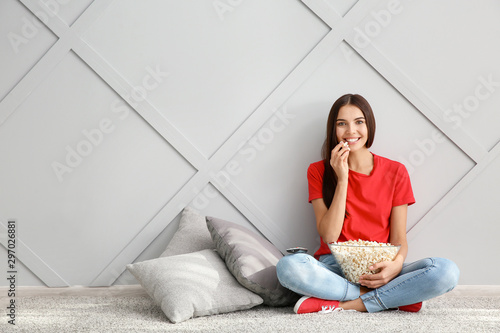 Young woman with popcorn watching movie near grey wall
